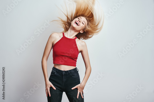 Feeling the freedom. Elegant and charming woman with long blond hair keeping eyes closed and smiling while standing against grey background
