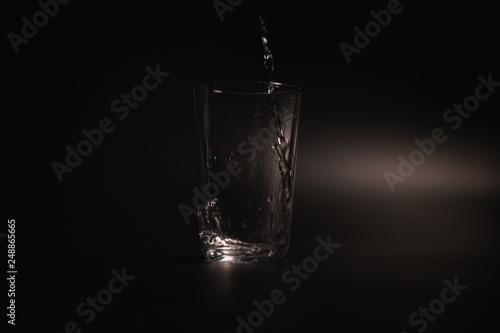 Water is poured into a transparent glass on a dark background