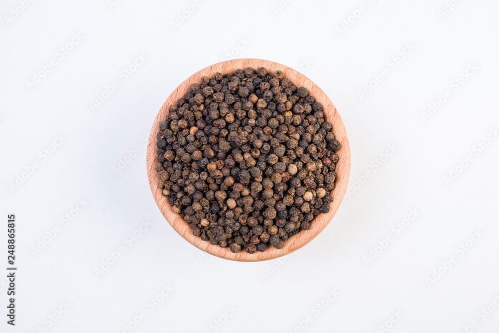 Black pepper peppercorns in wooden bowl isolated on white background. Top view. Black pepper peppercorns in wooden bowl isolated on white background. Top view.