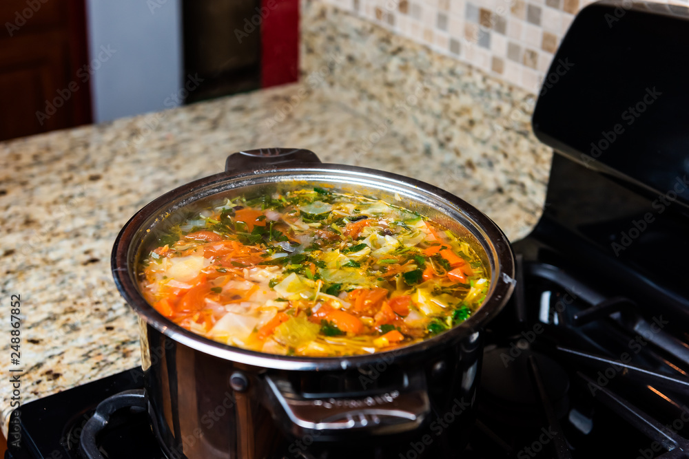 Large big pot of homemade vegetable soup and granite counter top in kitchen  in stainless steel container on gas stove cooking and nobody Stock Photo