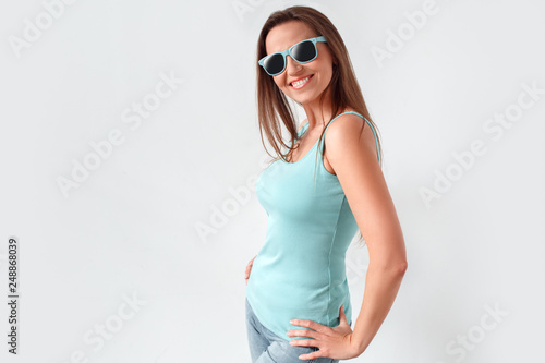 Freestyle. Woman in sunglasses standing studio isolated on white posing to camera happy side view