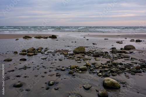 Ostsee Küste bei Ebbe, mit vielen Steinen am Sandstrand am späten bewölkten Nachmittag