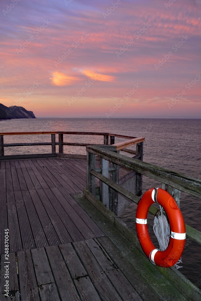 Wooden pier with a red lifebuoy on the Baltic Sea after sunset, overlooking the sea with copy space