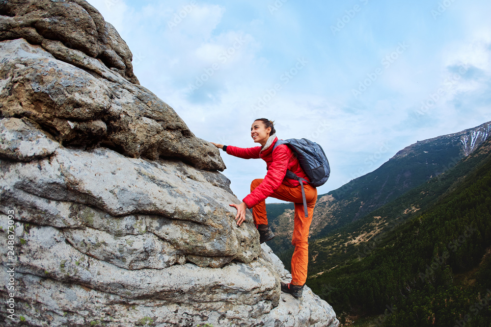 smiling and cheerful young woman is climbing by the edge of a cliff