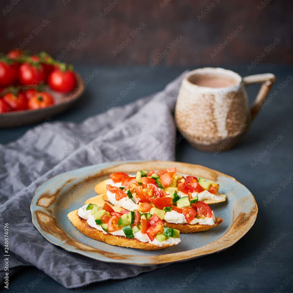 Three crostini, traditional Italian sandwich with tomatoes and cucumbers. Breakfast on plate, Cup of cocoa, dark background, side view Three crostini, traditional Italian sandwich with tomatoes and cucumbers. Breakfast on plate, Cup of cocoa, dark background, side view