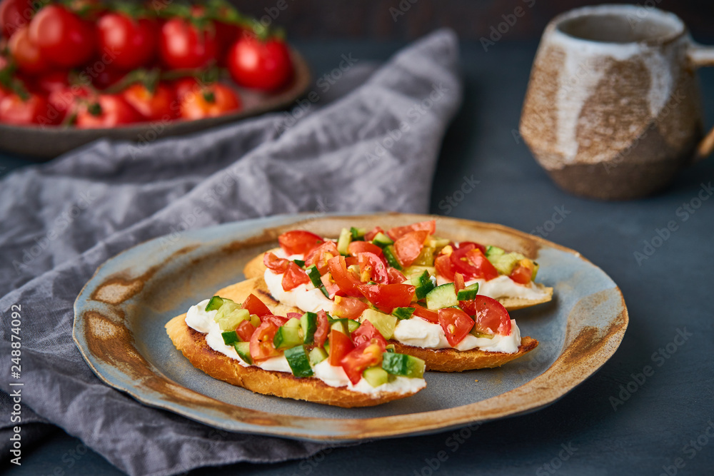 Three crostini, traditional Italian sandwich with tomatoes and cucumbers. Breakfast on plate, Cup of cocoa, dark background, side view