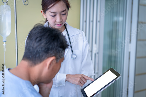 Woman doctors are explaining something from a tablet to a sick male patient. © amornchaijj