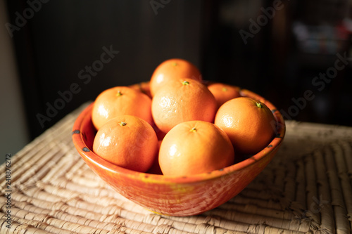 Pomarańczowa ceramiczna miska z mandarynkami na słomkowej macie