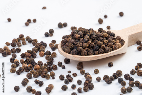 blask pepper peppercorns in wooden spoon isolated on white background. Closeup.