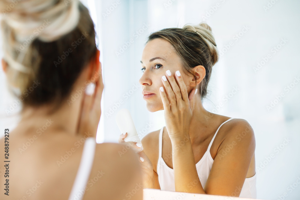 Woman applying face cream in bathroom Woman applying face cream in bathroom