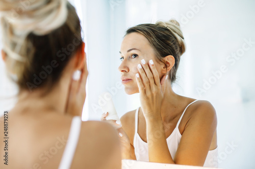 Woman applying face cream in bathroom