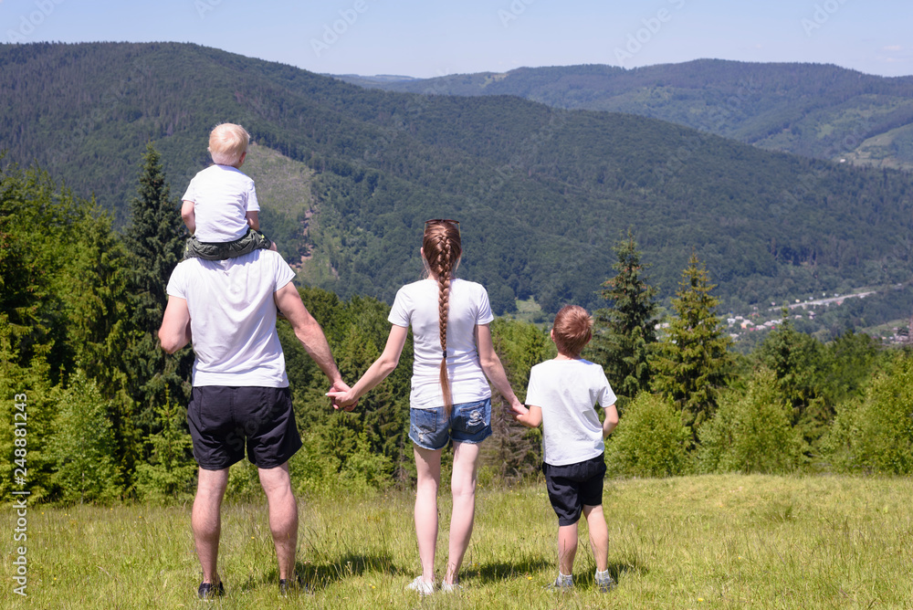 Father, mother and two little sons are standing on a green field on a background of wooded hills. Family values