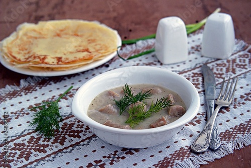 Machanka, thick sauce on meat broth with homemade pork sausages in a white bowl. Served with thin wheat pancakes. Belarusian cuisine photo