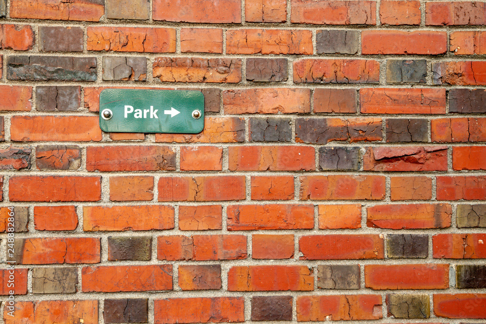 Background image of a rustic red brick wall with a sign pointing to a park Background image of a rustic red brick wall with a sign pointing to a park