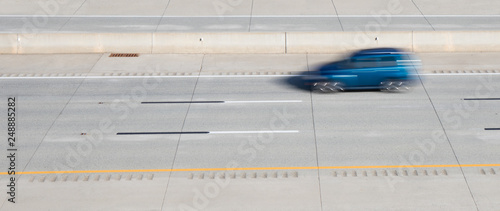 A blurred motion photo of a blue car on a highway.