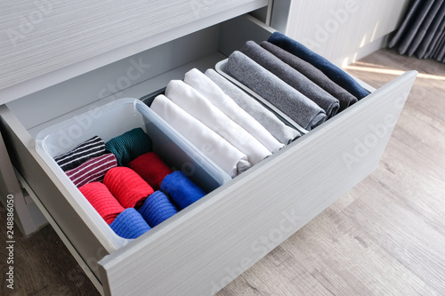 Close up stack of folded t shirt black gray white color and folded bright colorful socks in plastic baskets in a closet drawer in natural light. Room cleaning and tidying up concept.