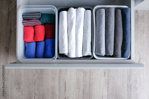 Close up stack of folded t shirt black gray white color and folded bright colorful socks in plastic baskets in a closet drawer in natural light. Room cleaning and tidying up concept. Top view.