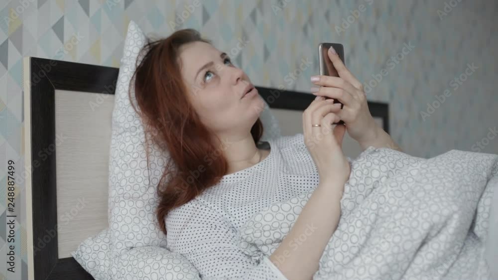 Beautiful and cheerful woman lying in bed at home and using smartphone having video chat with friends enjoying online communication Beautiful and cheerful woman lying in bed at home and using smartphone having video chat with friends enjoying online communication