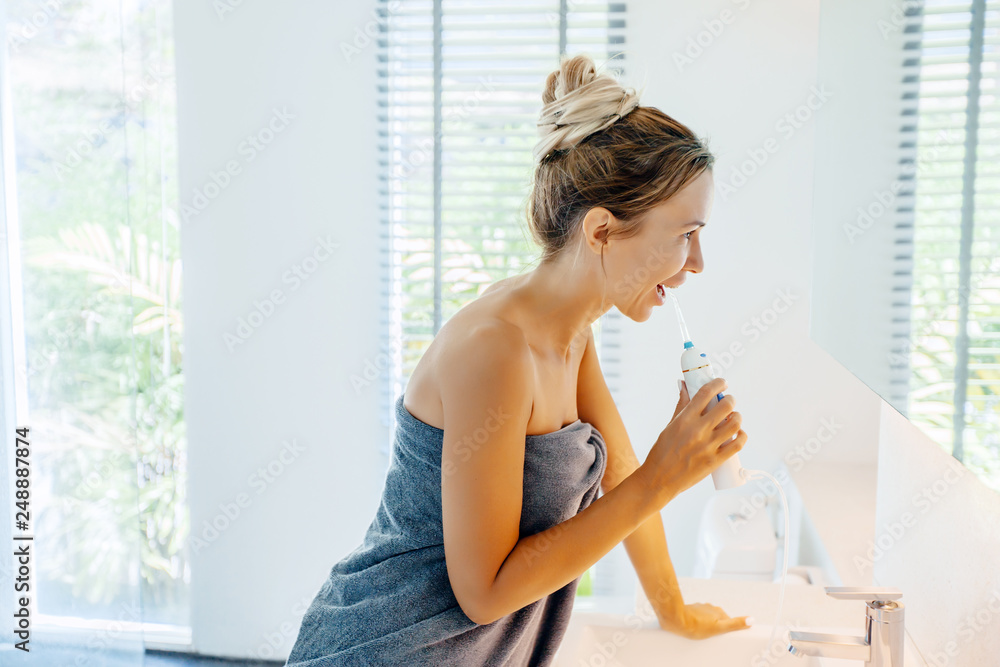 Woman brushing teeth with water floss in bathroom Woman brushing teeth with water floss in bathroom