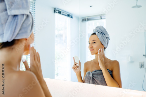 Woman applying face cream in bathroom