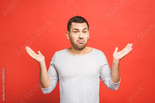 Confused embarrassed attractive adult man with bristle, shrugging with raised palms, smiling nervously, feeling guilty over red background. Oops, my bad. It was my fault