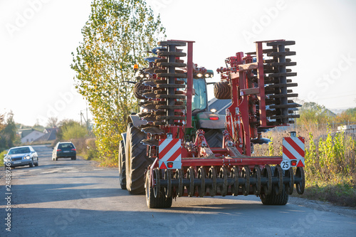Tractor combine with disc harrows driving along rural road on sunny day. Agricultural machinery and farming concept.
