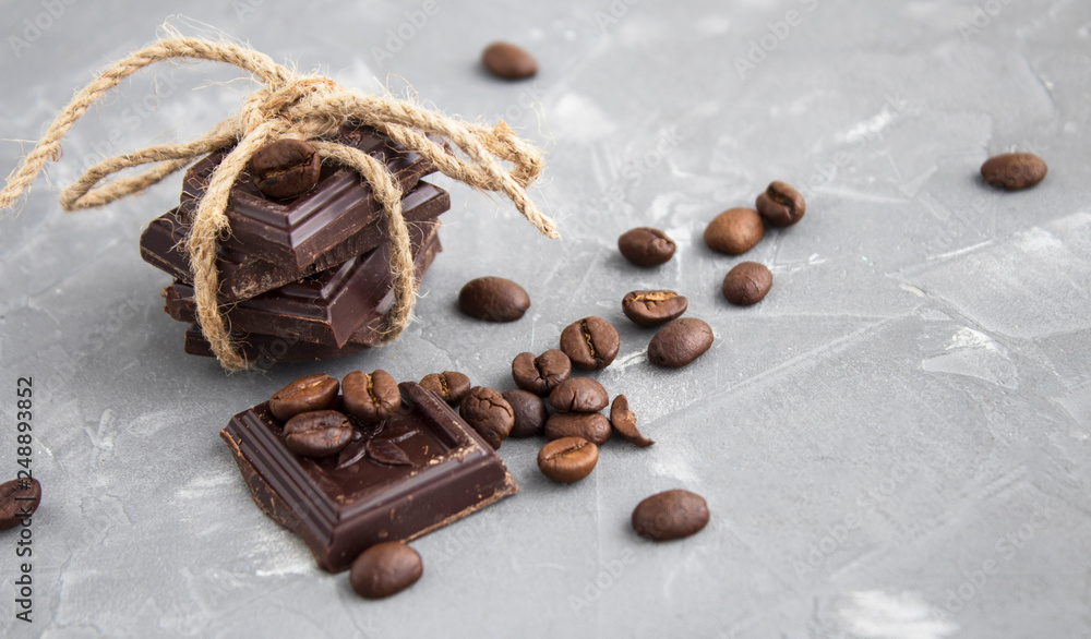 three thick pieces of chocolate tied by a linen rope and coffee beans, soft focus, on a gray background three thick pieces of chocolate tied by a linen rope and coffee beans, soft focus, on a gray background