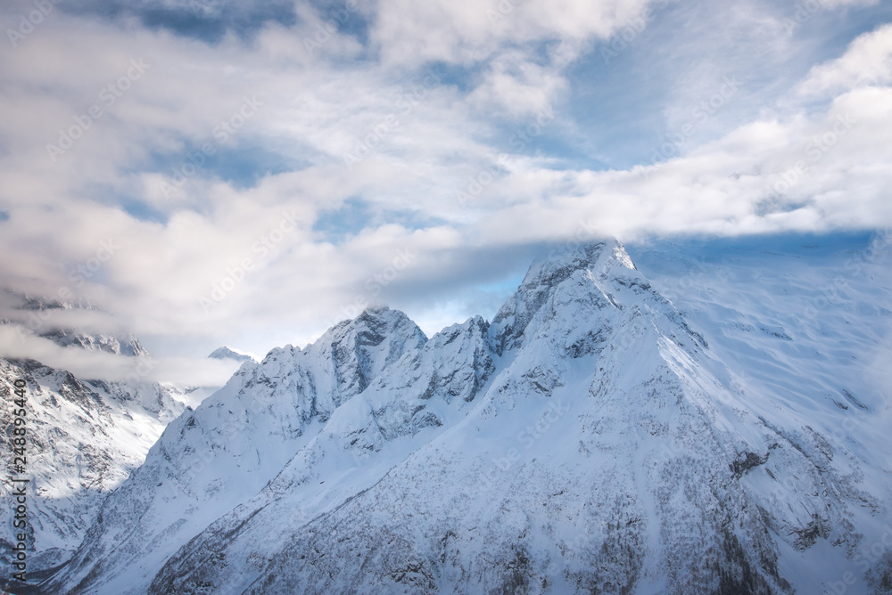 mountain peaks of Dombai mountains covered with snow surrounded by thick clouds against the blue sky. February 2019