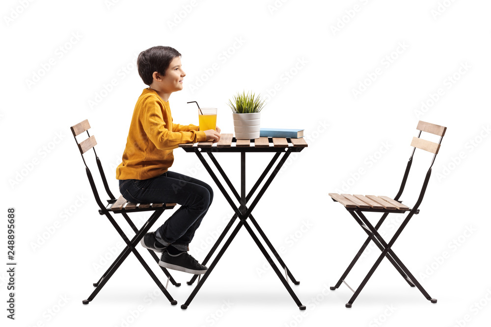Fototapeta premium Little boy sitting alone at a table with orange juice