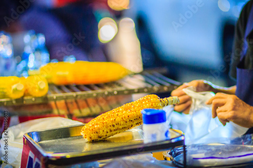 Close up hand of street food vendor while grilling and selling for mixed sweet corn butter. Cook is selling grilled sweet corn on street in Bangkok night market, Thailand.