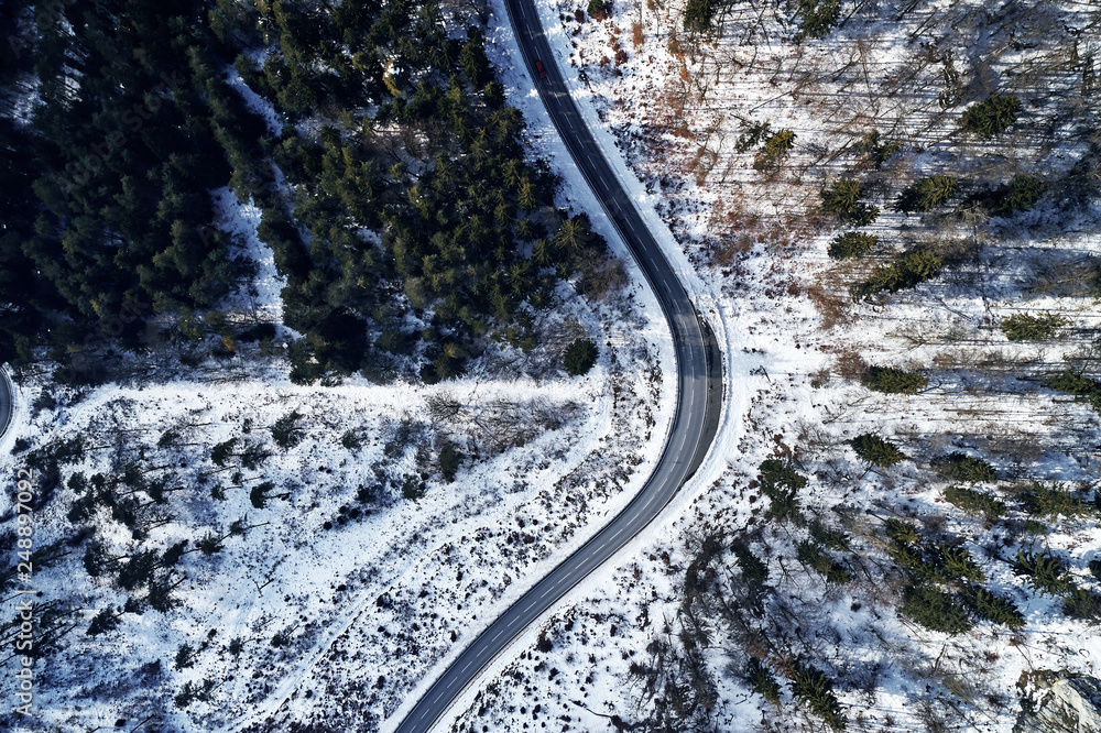 curved road in winter mountain landscape. Aerial view of forest and trees with a winding street surrounded by snow.