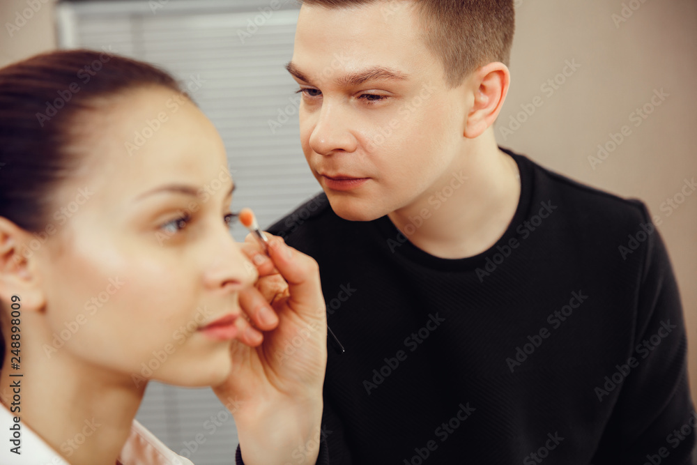 Professional makeup artist working with beautiful young woman. The man in female proffesion. gender equality concept Professional makeup artist working with beautiful young woman. The man in female proffesion. gender equality concept