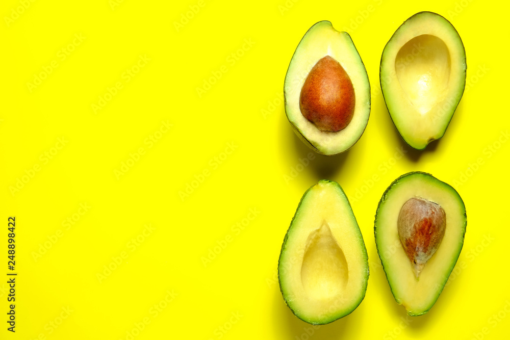 Minimal composition with halved nutrient dense avocado fruit slices full of heart healthy monounsaturated fat on bright yellow background with copy space for text. Close up, top view.