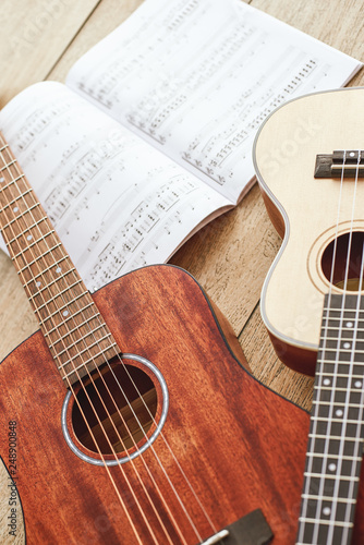 Learning how to play guitar. Vertical close up photo of acoustic and ukulele guitars lying on the wooden floor with music notes.