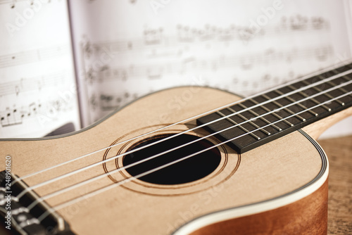 Ukulele chords. Close-up photo of ukulele guitar and music notes against of wooden background. Musical instruments. Music equipment