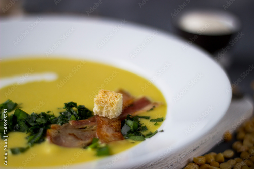 Pea soup with pieces of bacon, parsley and onion in a bowl on a dark background. Pea cream soup. Macro. Pea soup with pieces of bacon, parsley and onion in a bowl on a dark background. Pea cream soup. Macro.