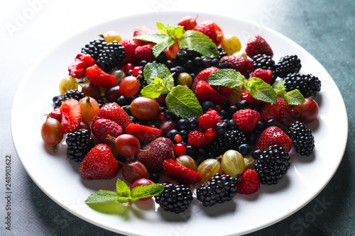 Fruit salad with raspberry  currant  strawberry  blueberries  gooseberries  blackberries and mint on a white plate.