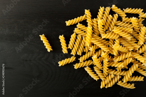 farfalle Raw Fusilli italian pasta on a wood black textured background. Close-up view from the top. Free space for text. photo