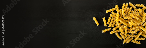 farfalle Raw Fusilli italian pasta on a wood black textured background. Close-up view from the top. Free space for text. banner