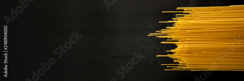 farfalle Raw spaghetti italian pasta on a wood black textured background. Close-up view from the top. Free space for text. Banner