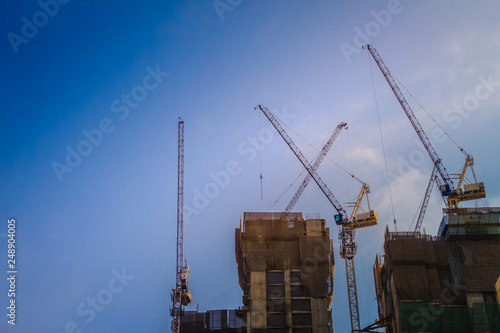Luffing jib tower crane at high rise building construction site project. Skyscraper building under construction with the tower cranes on top under the dramatic sky background.