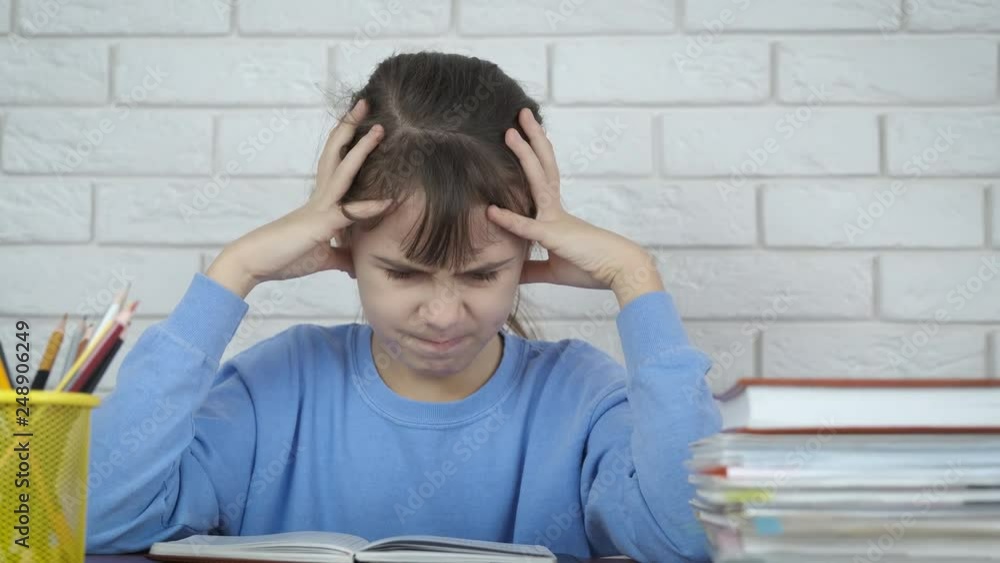 The child is nervous because of homework. A little girl holds her head looking at a school notebook. Concept with a problem in teaching a child. The child is nervous because of homework. A little girl holds her head looking at a school notebook. Concept with a problem in teaching a child.