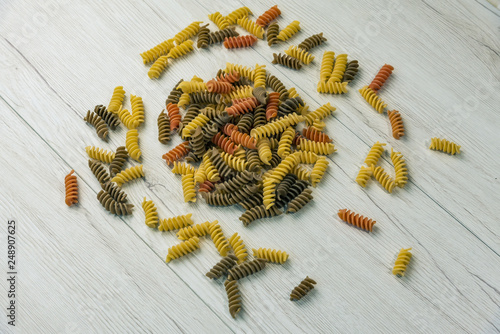Raw uncooked three-colored Fusilli on white wood table.