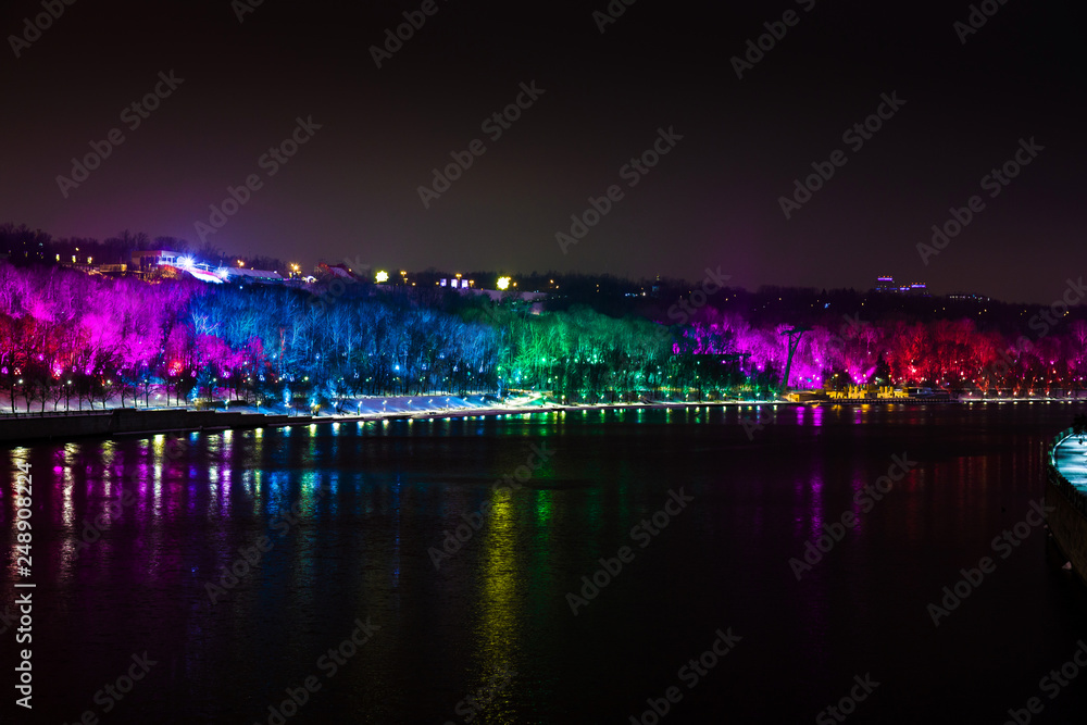 Colored illuminated trees by the river. Russia, Moscow.