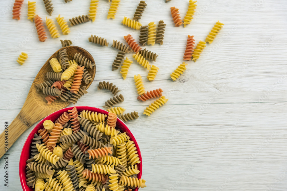 Fototapeta premium Raw uncooked three-colored Fusilli on white wood table.