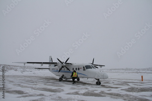 A small plane found on a tarmac in the late morning with snow on the ground being readied for takeoff in a remote northern community