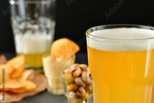 two glasses of beer and snacks chips, nachos with sauce, pistachios and salami, aperitif, relax in the bar with friends, beer party. selective focus and copy space