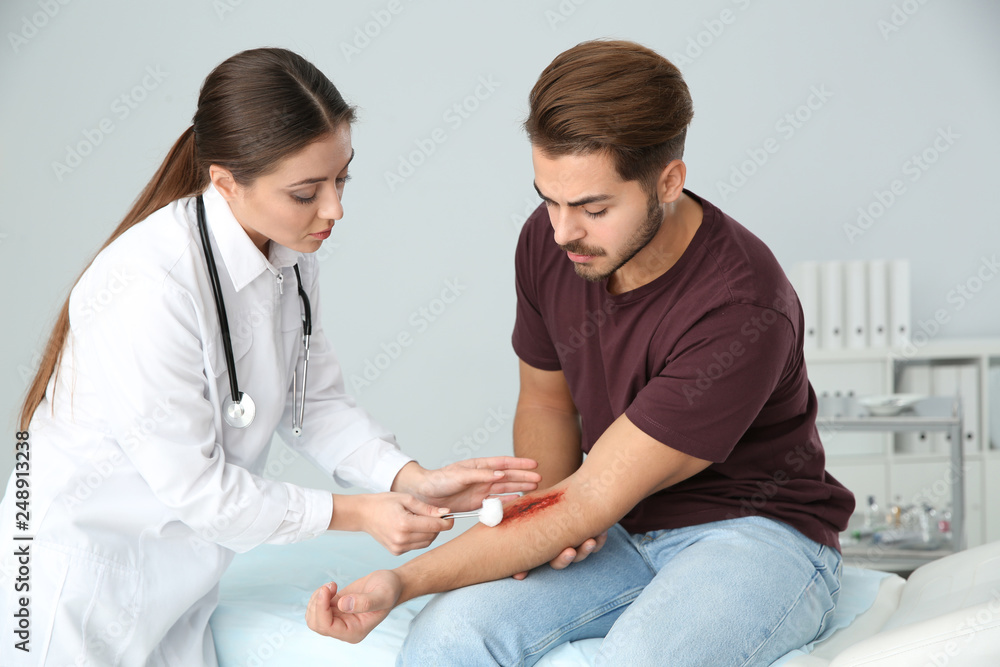 Female doctor cleaning young man's arm injury in clinic. First aid Female doctor cleaning young man's arm injury in clinic. First aid