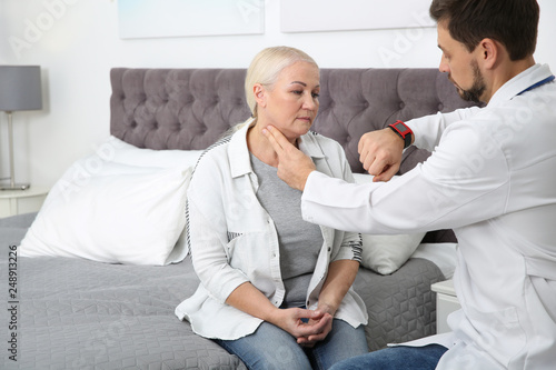 Doctor checking mature woman's pulse with fingers in bedroom