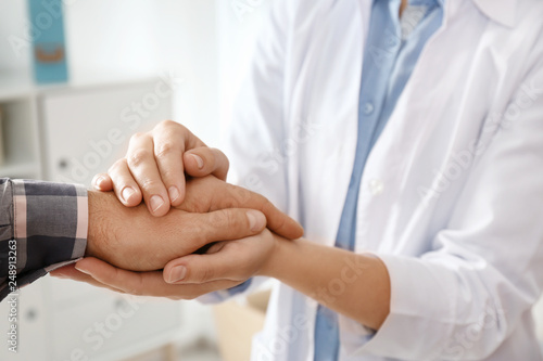 Female doctor comforting man on blurred background, closeup of hands. Help and support concept